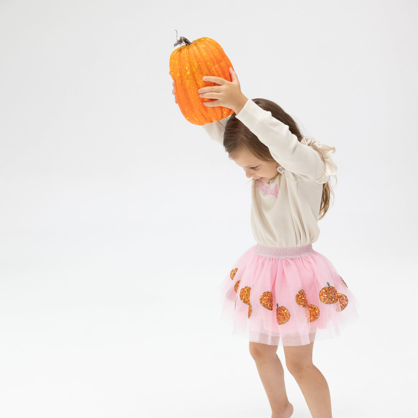 girl in a tutu skirt holding a pumpkin above her head