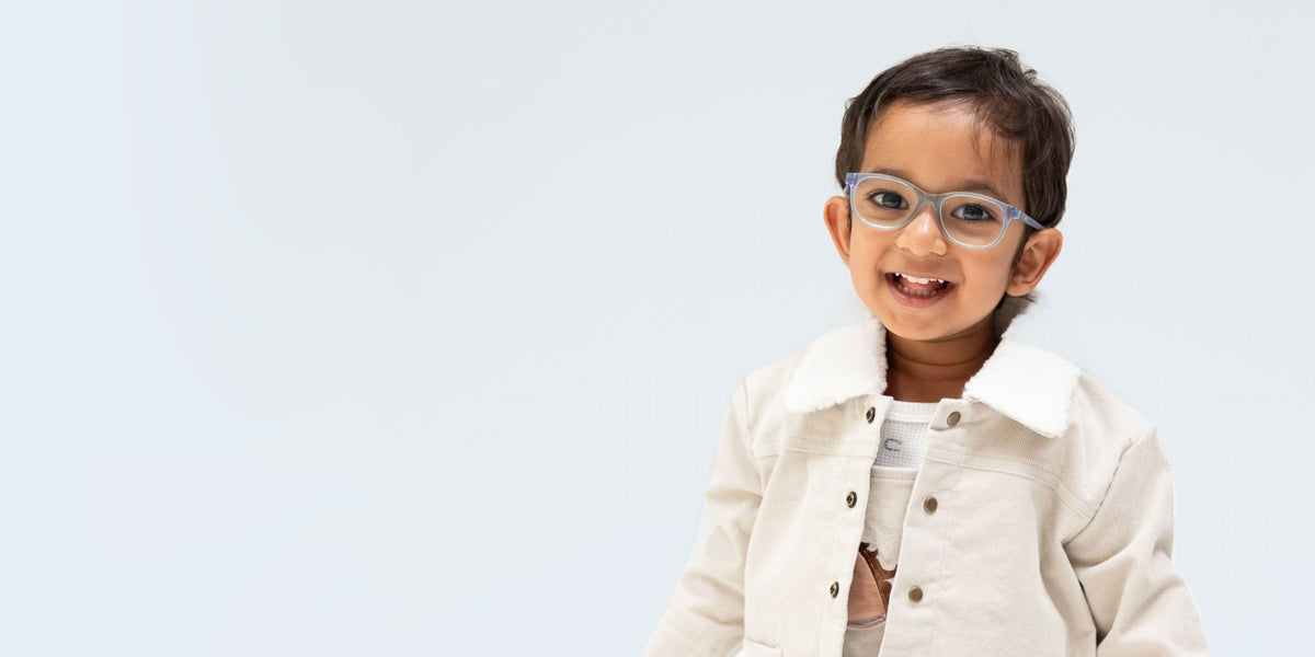 Toddler boy wears off whote corduroy overalls with a horses head appliqued at chest and a cordroy jecket of the same color with white sherpa fabric on the collar. He also wears light blue eyeglasses.