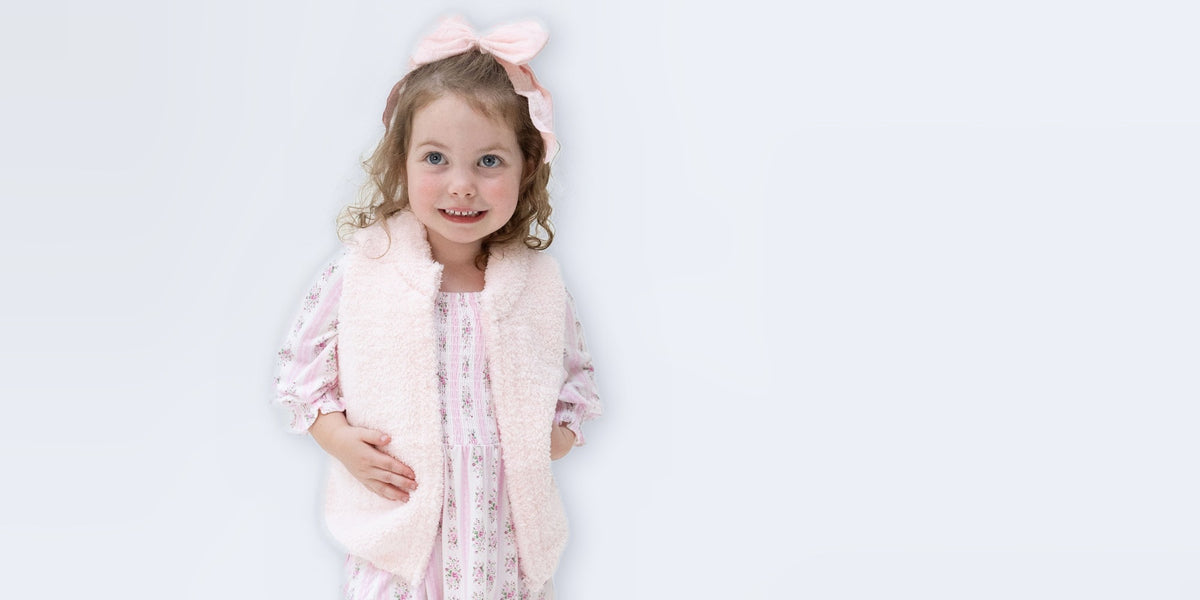 toddler girl wear a floral striped bamboo dress and light pink chenille vest on light blue background.