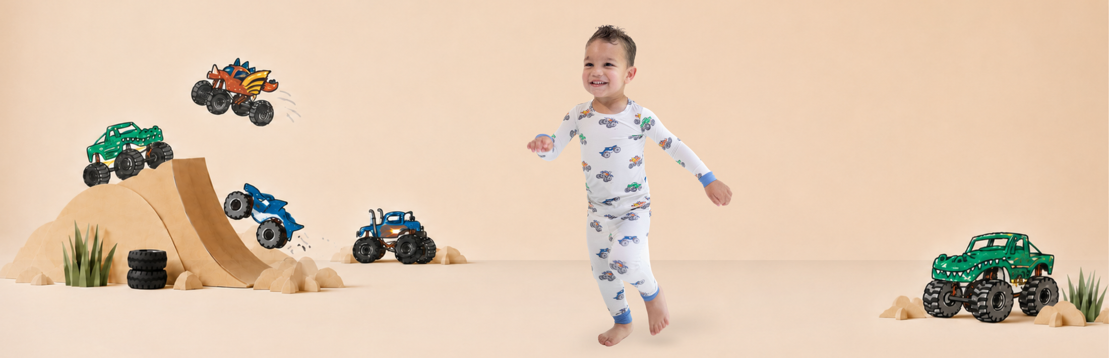 Boy wears pajama set with monster truck print as he runs through a photography set with wooden ramps and overlayed monster truck illustrations taken from the print he is wearing.