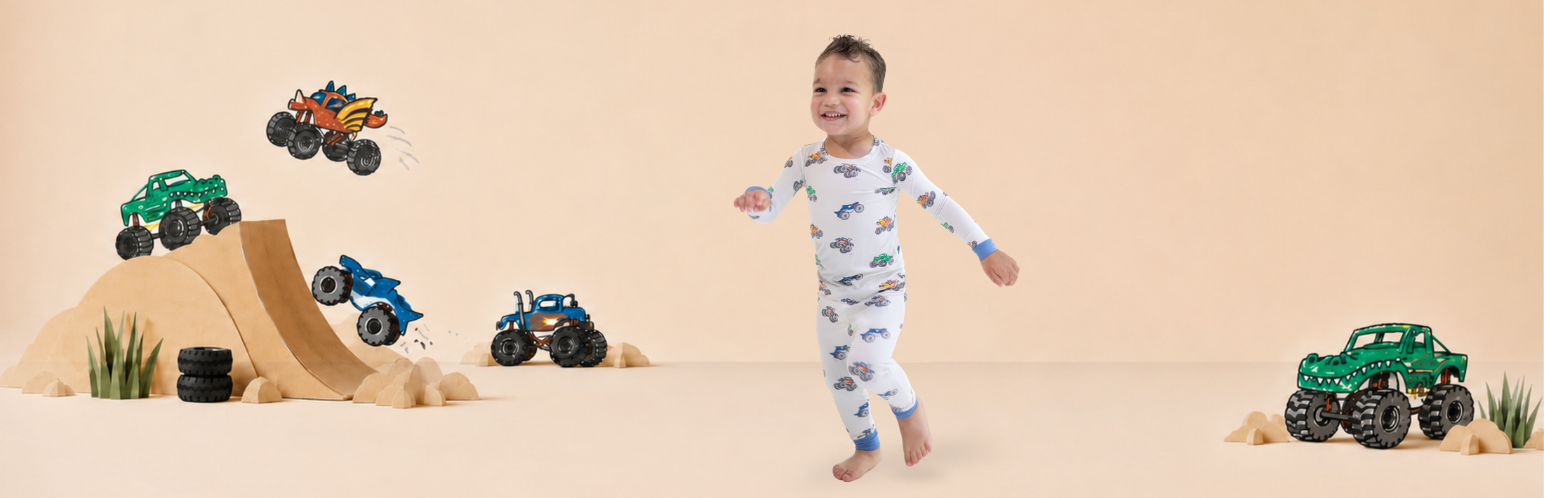 Boy wears pajama set with monster truck print as he runs through a photography set with wooden ramps and overlayed monster truck illustrations taken from the print he is wearing.