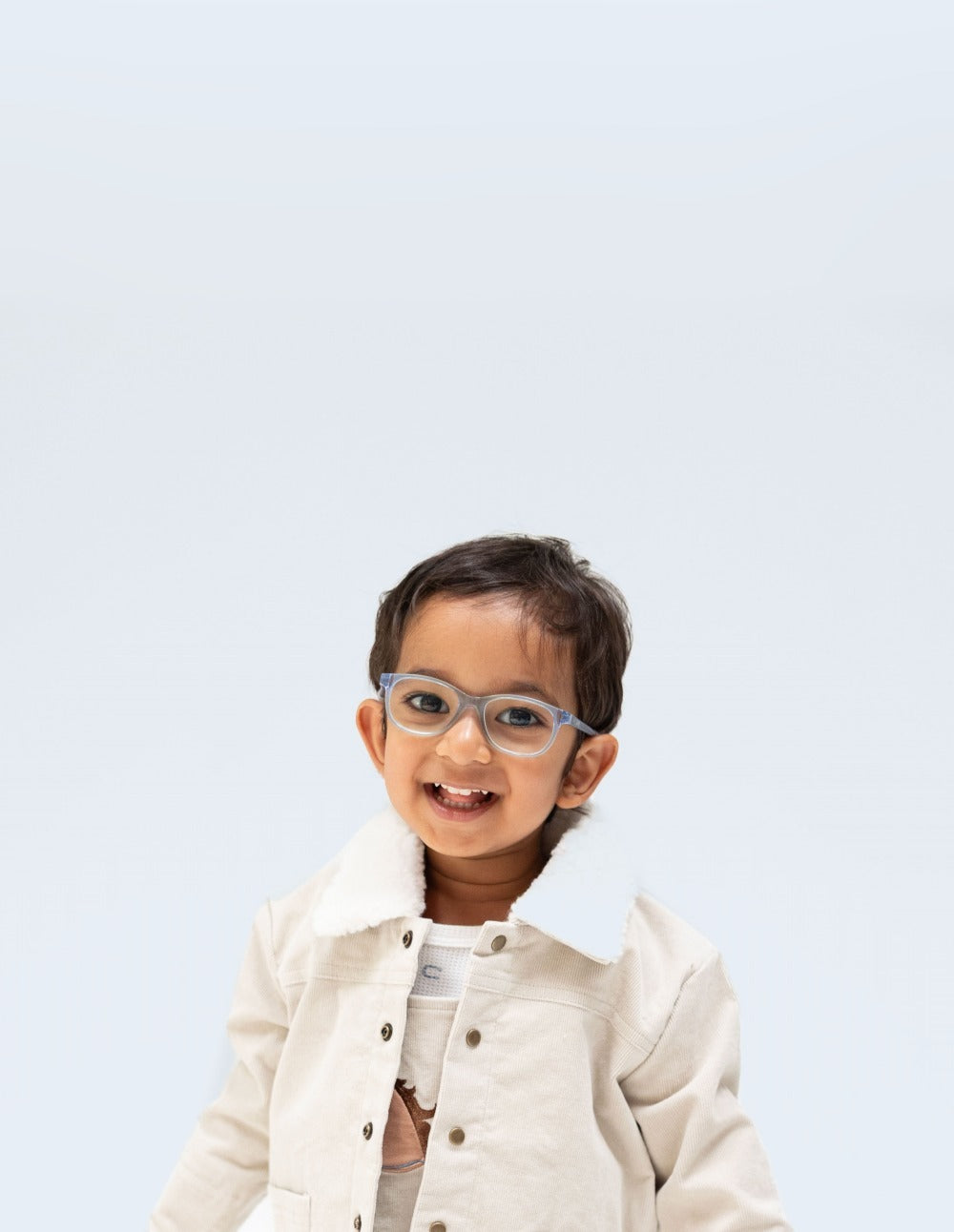 Toddler boy wears off whote corduroy overalls with a horses head appliqued at chest and a cordroy jecket of the same color with white sherpa fabric on the collar. He also wears light blue eyeglasses.