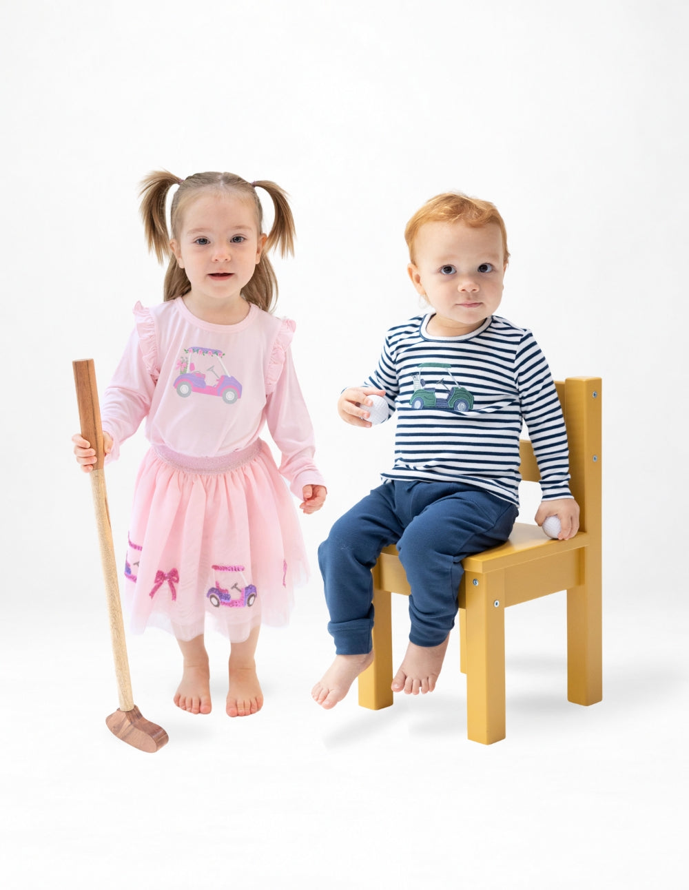 Girl and boy toddler wear golf play wear. The girl is wearing a long sleeved pink shirt with ruffles at the shoulder and a golf cart on the chest paired with a golf tutu. The boy wears a classic navy and white striped long sleeve shirt with a green golf cart applique on the chest paired with navy french terry jogger pants.
