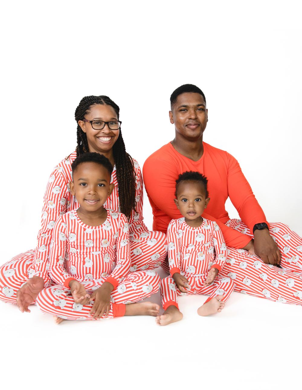 A family wears matching holiday pajamas in a red and white stripe with vintage Santa Claus face print.
