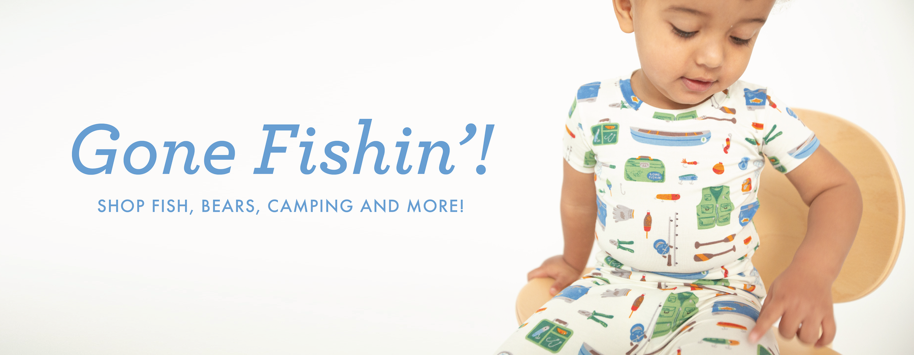 Toddler boy points to fishing tools print on pajamas. Text says Gone Fishin' Shop fish, bears, camping and more!