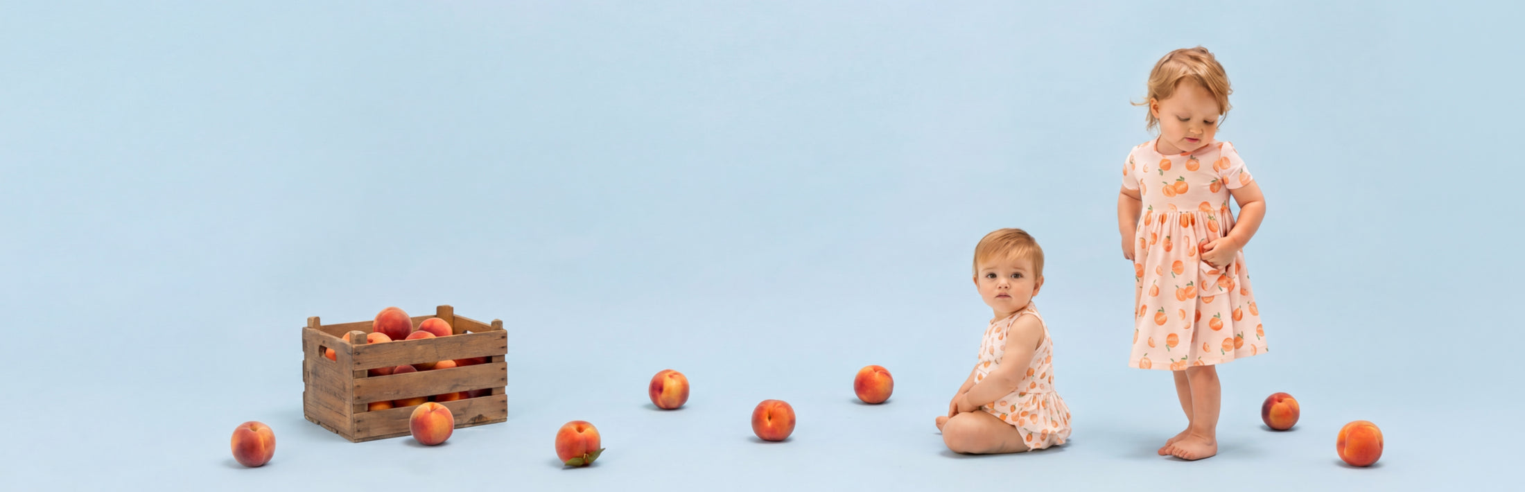 Two toddlers wear Peach printed outfits with peaches around the set on a light blue background.