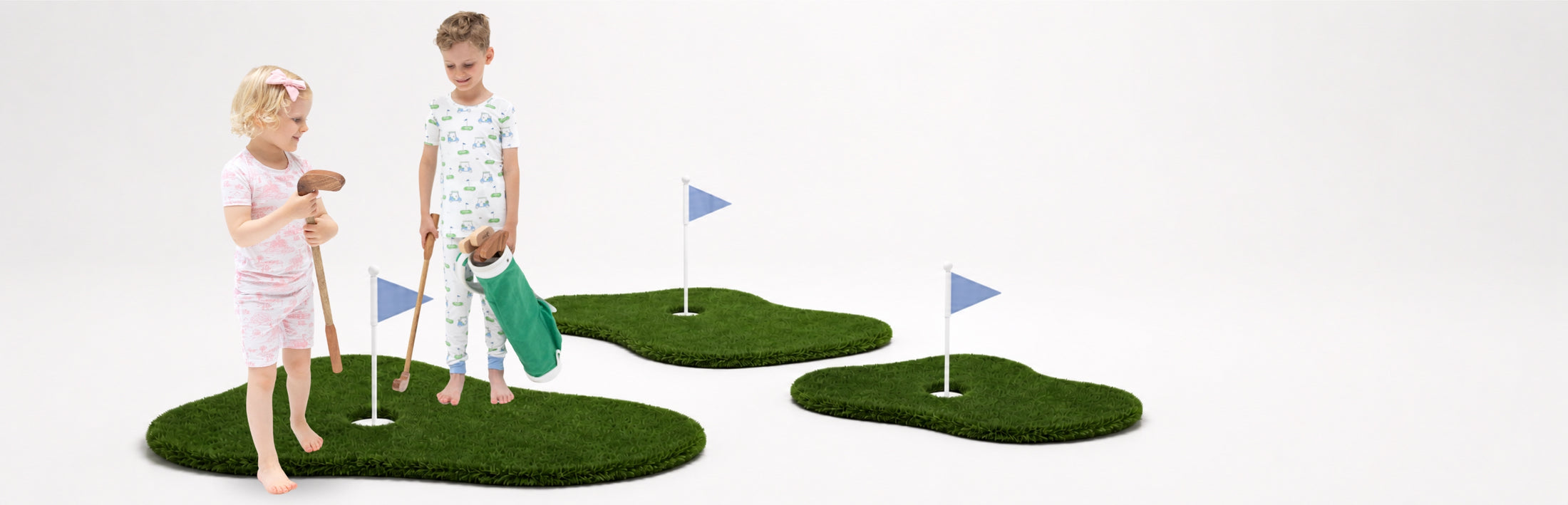 Two children wearing golf printed pajamas playing on small artificial grass golf greens with golf clubs and flags against a plain white background.