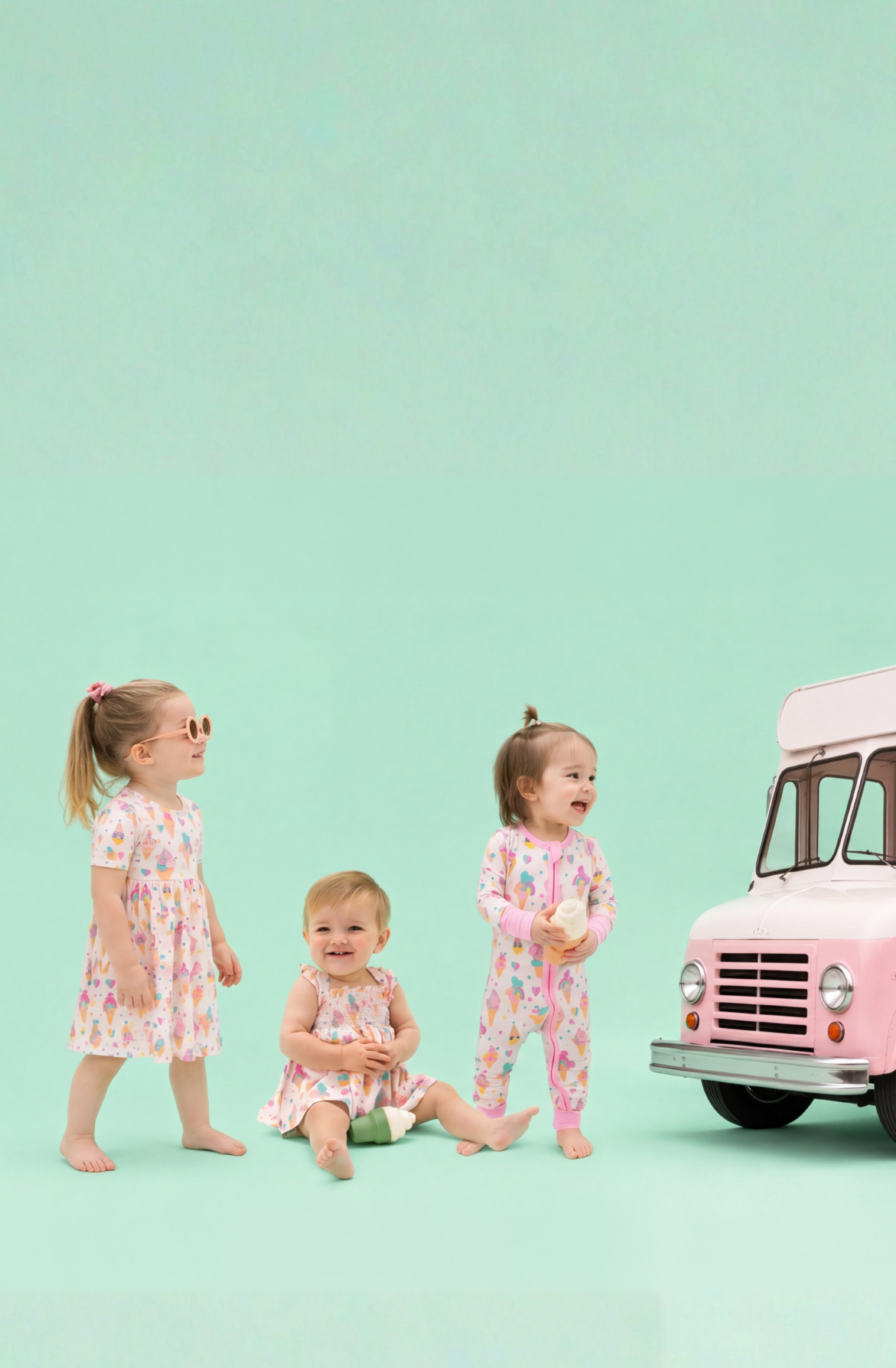 Three children in ice cream printed outfits standing next to a pink ice cream truck on a light green background
