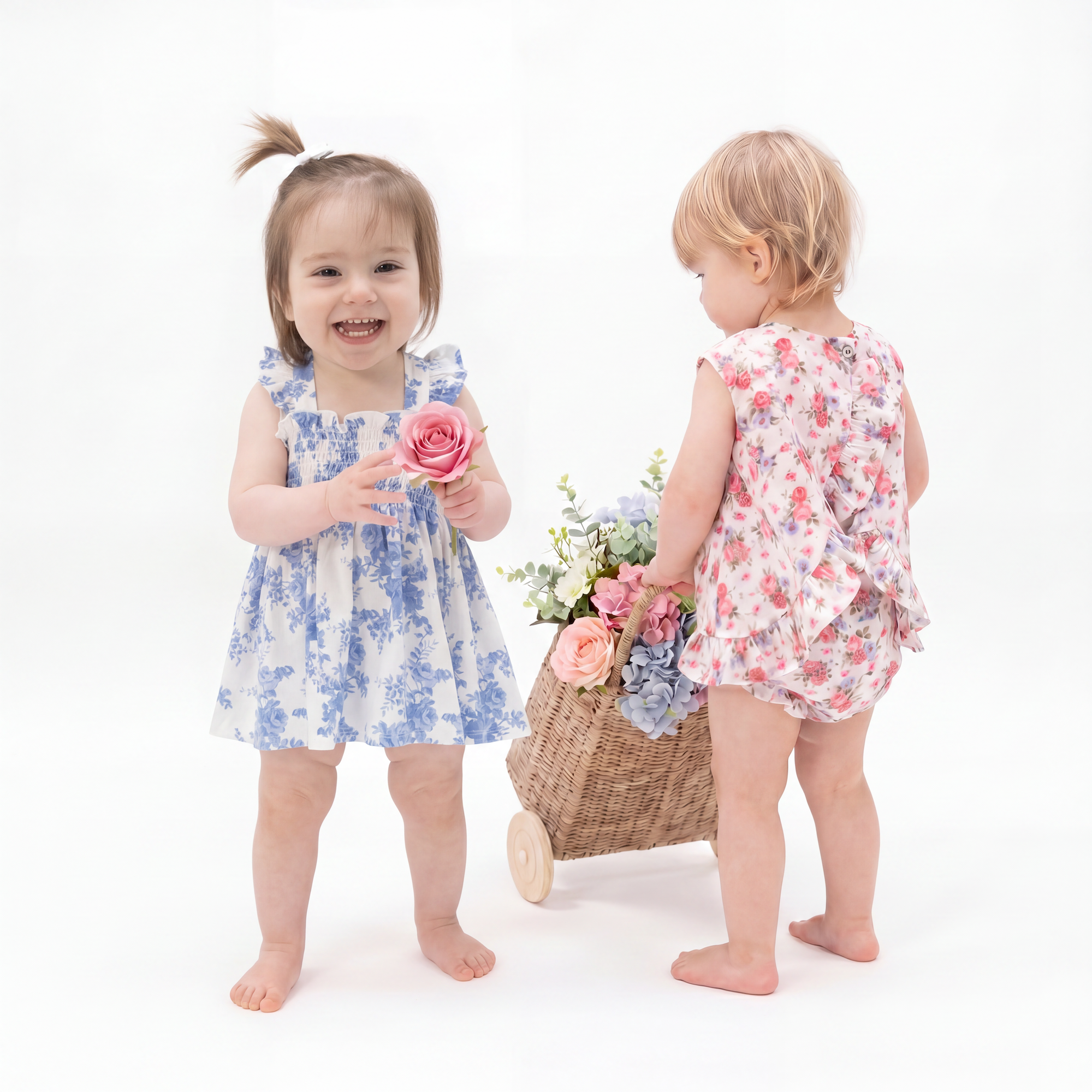 Two toddler girls wearing floral outfits with flowers and a basket on a white background