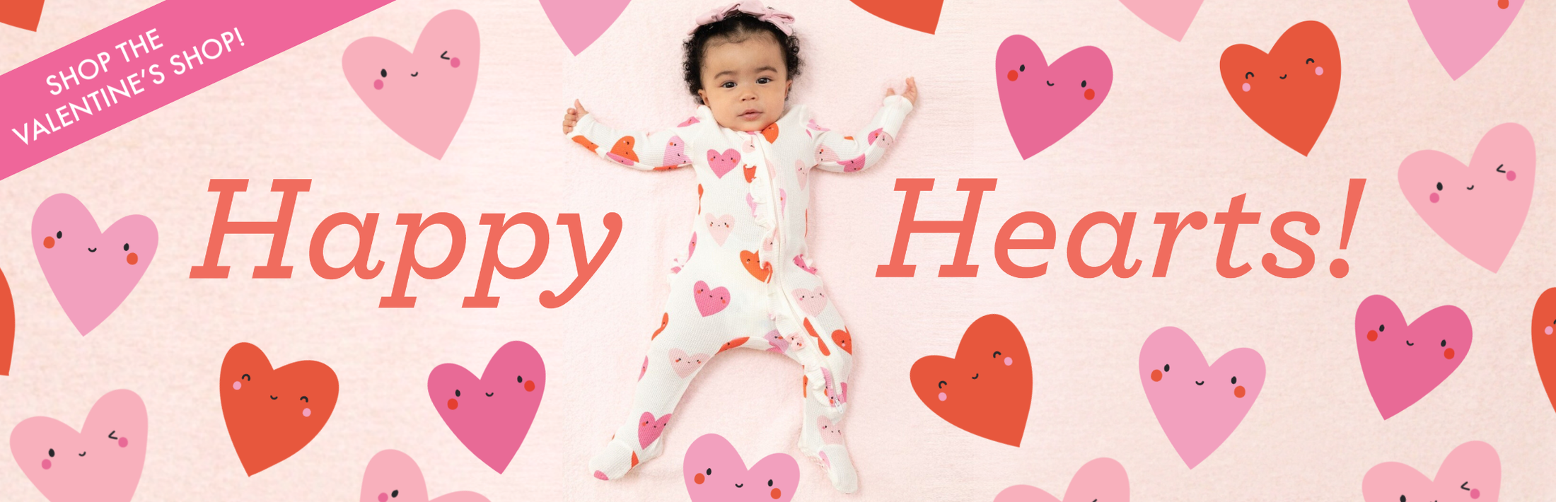 A baby girl lies on a light pink blanket wearing a zipper footie in the Happy Hearts print. Text reads, "Happy Hearts!! Secondary banner reads, "Shop the Valentine's Shop!"