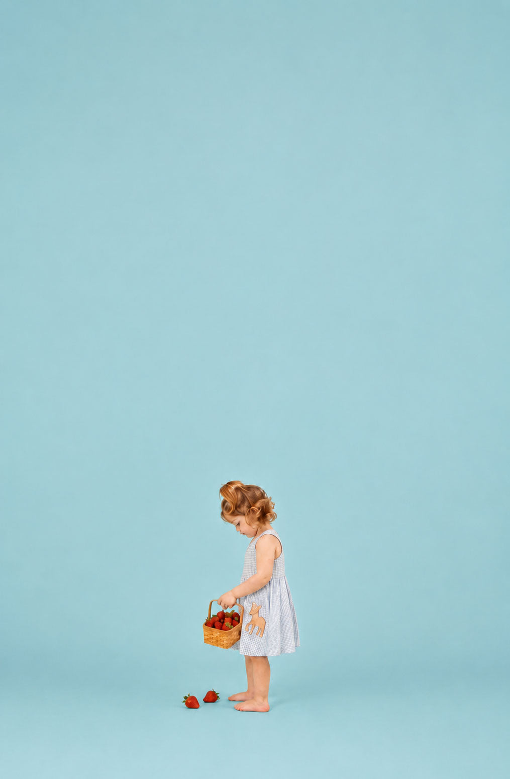 Young girl in a white dress holding a basket of fruit against a light blue background