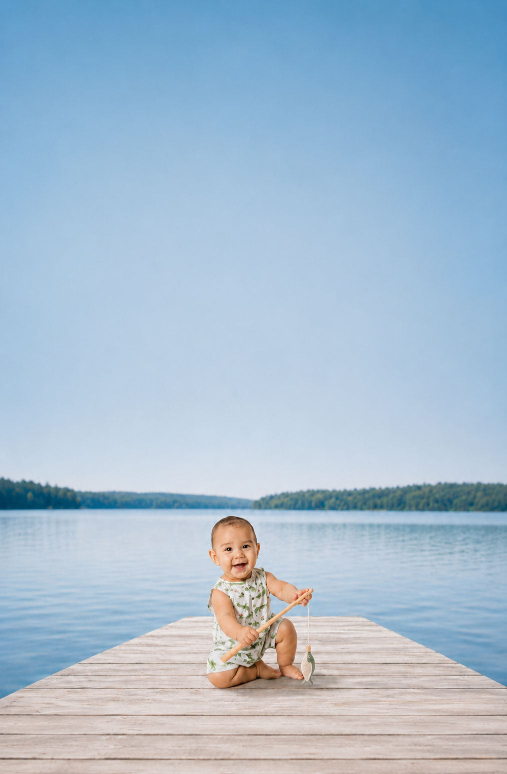 Baby sitting on a dock by a lake with clear blue sky