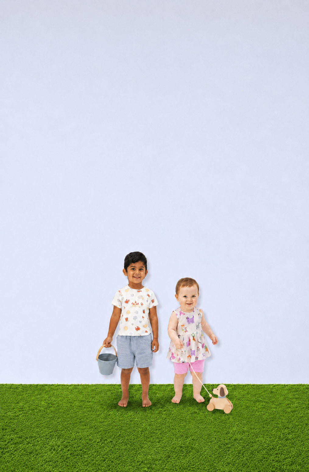 Two children standing on grass with a plain background