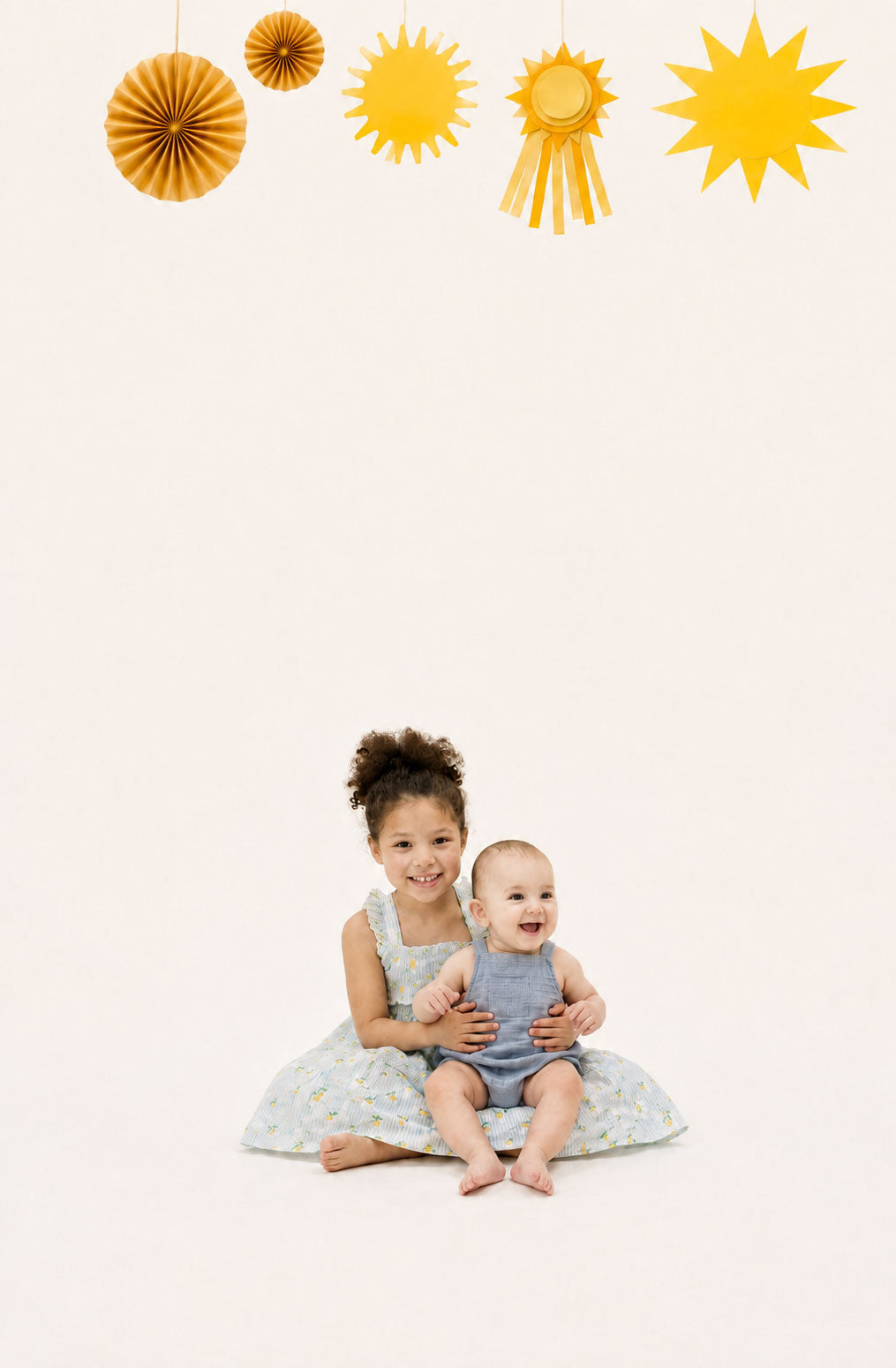 Two children sitting together with decorative suns and paper fans on a light background